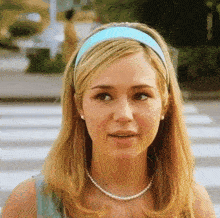 a woman wearing a blue headband and pearls looks at the camera
