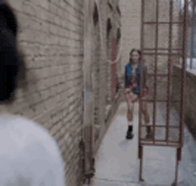 a woman is standing in a narrow alleyway next to a brick wall and a cage .