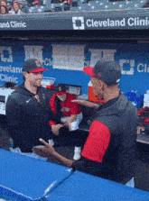 two baseball players are talking in a dugout with a banner that says cleveland clinic