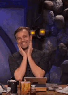 a man is sitting at a desk with his hands on his face and smiling