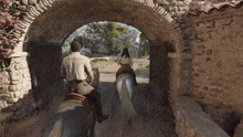 a man and woman are riding horses through an archway