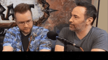 two men are talking into microphones in front of a sign that says " ra "