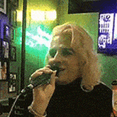 a woman is singing into a microphone in a room with a green light behind her .