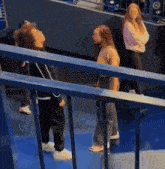 a group of people are standing on a blue floor behind a railing