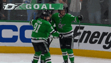 two ice hockey players are celebrating a goal in front of a banner that says goal