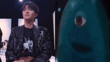 a man in a black jacket is sitting in front of a blue monster with a big eye .