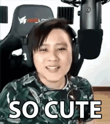 a man is sitting in a chair in front of a microphone with the words `` so cute '' written on his face .