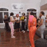 a group of women are dancing in a living room and one woman is wearing a pink hoodie