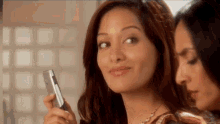 a woman is holding a cell phone and smiling while another woman looks on