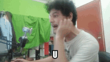 a man is sitting in front of a green screen with the letter u above his head