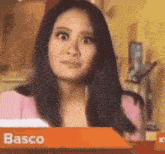 a woman in a pink jacket is making a funny face while standing in front of a sign that says basco .