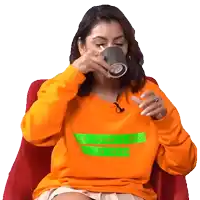 a woman wearing an orange sweater that says ' the judge & the lover ' on it is drinking from a cup