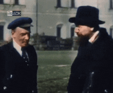 two men are talking in front of a building with a 24 ack sticker on it