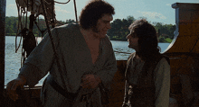 two men on a boat talking to each other with a lake in the background