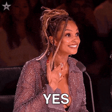 a woman with dreadlocks is sitting in front of a microphone and smiling while saying yes