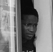a black and white photo of a man peeking out of a doorway .