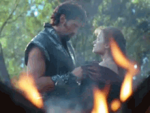a man and woman are standing in front of a fire .