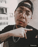 a man wearing glasses and a hat is pointing at the camera with the word tenada below him