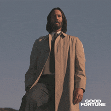 a man in a trench coat stands in front of a blue sky with the words good fortune below him