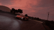 an orange sports car is driving down a road at sunset