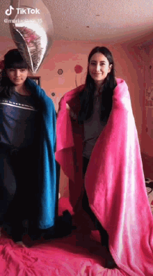 two girls are wrapped in blankets and a balloon .