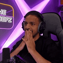 a man wearing headphones covering his mouth in front of a sign that says the hefz
