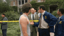 a man in a blue jacket with the letter t on it talks to another man