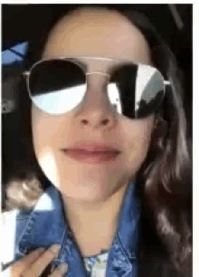 a woman wearing sunglasses and a denim jacket is smiling .