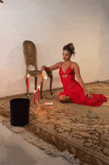 a woman in a red dress is kneeling in front of a chair with candles