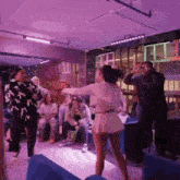 a group of people are dancing in a room with purple lights