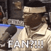 a man wearing a headband and glasses is sitting in front of a microphone and saying `` fan ? '' .