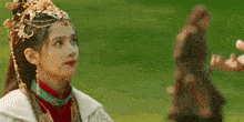 a woman in a traditional costume is standing in a field with a man in a blurred background .