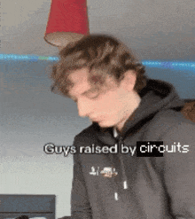 a man wearing a black hoodie with the words " guys raised by circuits " written on it