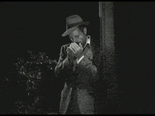 a man in a hat is covering his mouth with his hands in a black and white photo