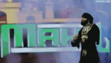a man with a beard is holding a wrestling championship while standing in front of a green and blue sign .