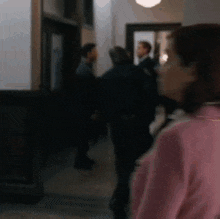 a woman in a pink sweater is standing in a hallway with a blurry background of people .