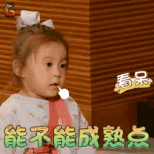 a little girl is holding a lollipop in her mouth with chinese writing on it