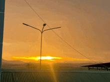 the sun is setting behind a street light