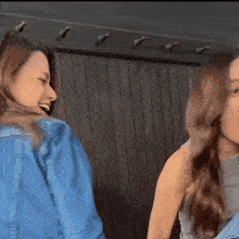 two women are standing next to each other in front of a wooden wall and laughing .