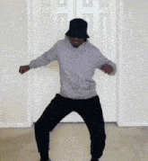 a man wearing a hat and a hoodie is dancing in front of a white door .