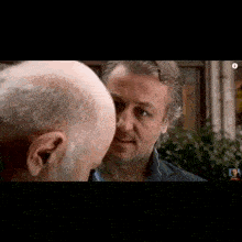 two men are looking at each other and one has a bald head .