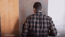 a man in a plaid shirt is standing in front of a door and looking out .