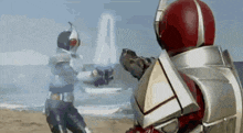 two kamen riders are fighting on the beach with a building in the background .