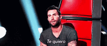 a man in a black shirt is sitting in a red chair and saying te quiero .