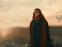 a man with red hair and a beard is standing in front of a mountain