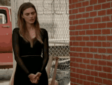 a woman in a black dress stands in front of a red truck