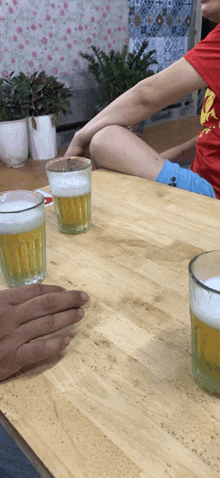 a person in a red shirt sits at a table with two glasses of beer