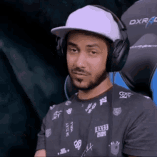 a man wearing headphones and a hat is sitting in a dxracer chair .