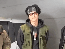 a young man wearing glasses and a bandana is standing in front of a van .