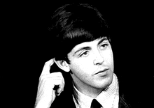 a black and white photo of a young man in a suit and tie holding his hand to his ear .